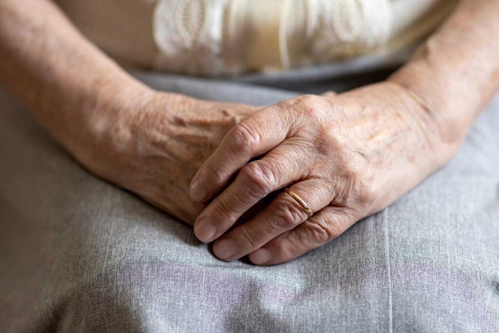 Older adults gather in a bright assisted living lounge with accessible seating, a dining table, and indoor plants.